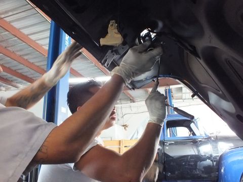 2003 Ford Crown Victoria - Pair of workers handle the inside of a black car's trunk lid, blue pickup in the shop