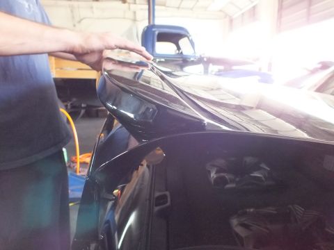 2003 Ford Crown Victoria - Hand steadies the black rear quarter panel of a car near a vintage blue pickup truck