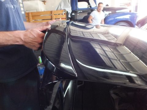 2003 Ford Crown Victoria - Glossy black rear fender and trunk seam of a car under garage lights, people behind