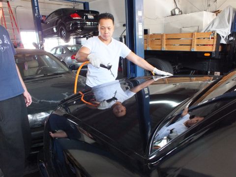 2003 Ford Crown Victoria - Worker cleans the roof of a black car on a lift, second black vehicle raised behind