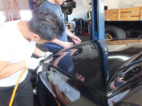 2003 Ford Crown Victoria - Technician works along the black roof and door panel of a car in a busy service bay