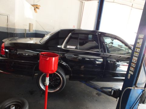 2003 Ford Crown Victoria - Side view of a black Crown Victoria on a lift, red drain funnel under the front wheel