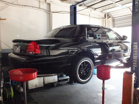 2003 Ford Crown Victoria - Black Crown Victoria sedan raised on a two-post lift, drain pans positioned beneath