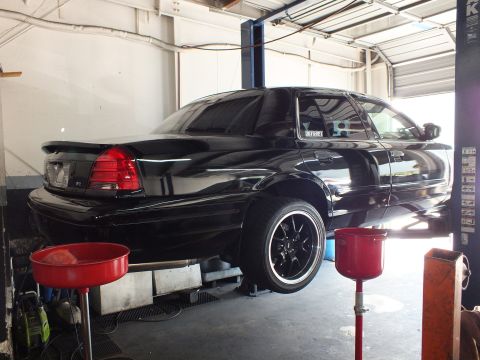 2003 Ford Crown Victoria - Rear quarter of a black Crown Victoria on a two-post lift inside a service garage
