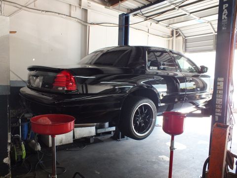 2003 Ford Crown Victoria - Rear three-quarter view of a black Crown Victoria sedan lifted on a two-post hoist in a garage bay
