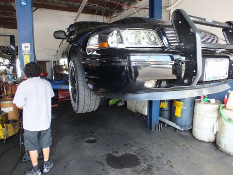 2003 Ford Crown Victoria - Worker beneath a black Crown Victoria raised on a hoist with chrome brush guard and black wheels