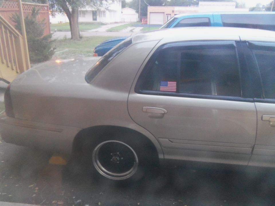 Gold sedan with black rims, American flag sticker on rear window, seen from the side