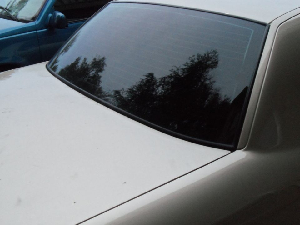 Rear window and trunk of a light-colored car, with a blue SUV visible in the background