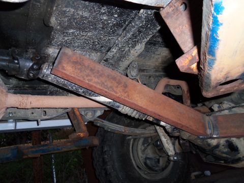 1989 Ford Bronco - A close-up view of the rear suspension system, showing a rusty metal reinforcement bar welded to the frame.