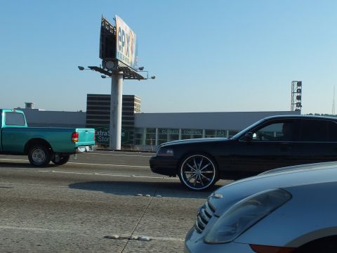 2003 Ford Crown Victoria - Lowered black Crown Victoria on chrome wheels driving past a teal pickup and storage building