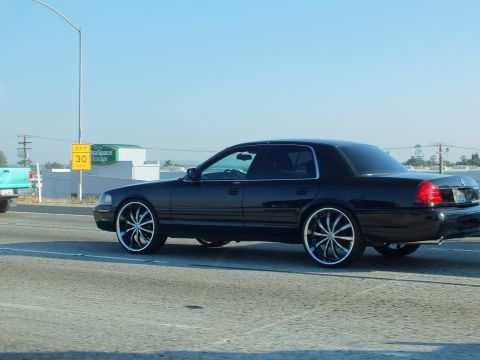 2003 Ford Crown Victoria - Side view of a black Crown Victoria riding on oversized chrome wheels along a roadway