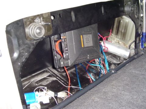 1999 Ford Taurus - A black car audio amplifier mounted to a board on the rear trunk wall, with orange power, blue and red speaker leads and a bundle of white…