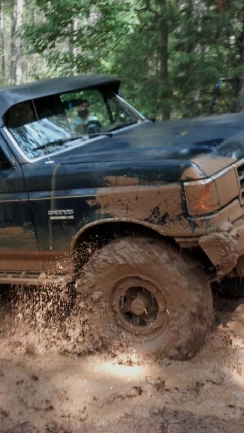 1990 Ford Bronco - This Bronco is deep in the mud, kicking up a spray as it drives through the off-road course.