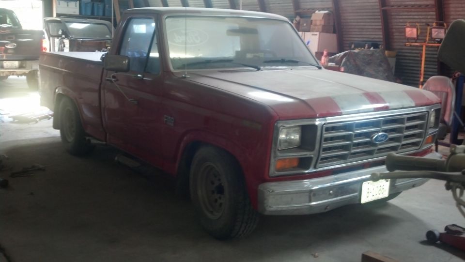 Red 1980s Ford F-Series single-cab pickup parked inside a shop or barn