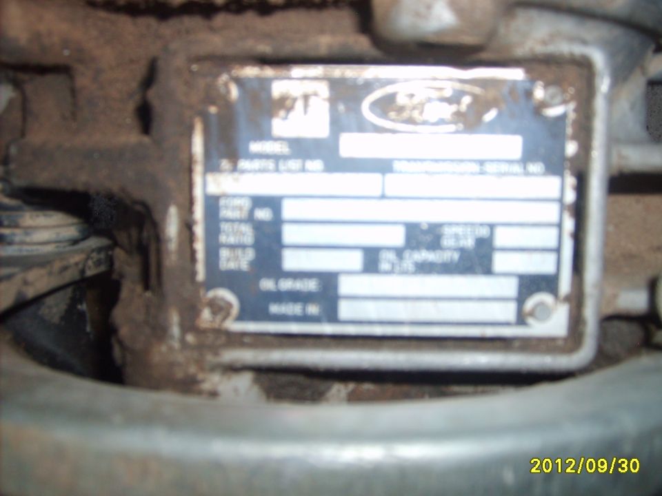 Blurry Ford transmission ID tag with model, serial and build date fields on a grimy transmission case