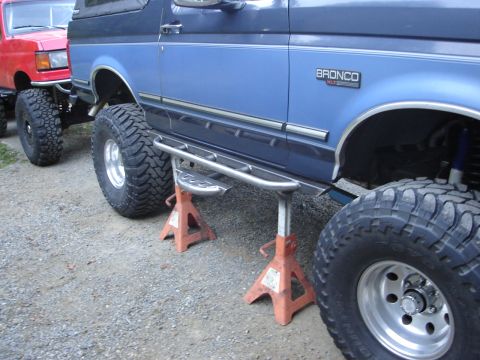 1989 Ford Bronco - Blue 1989 Ford Bronco with aftermarket side steps is on jack stands next to a red truck.
