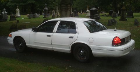 1998 Ford Crown Victoria - A white sedan is parked on a paved path in a cemetery.