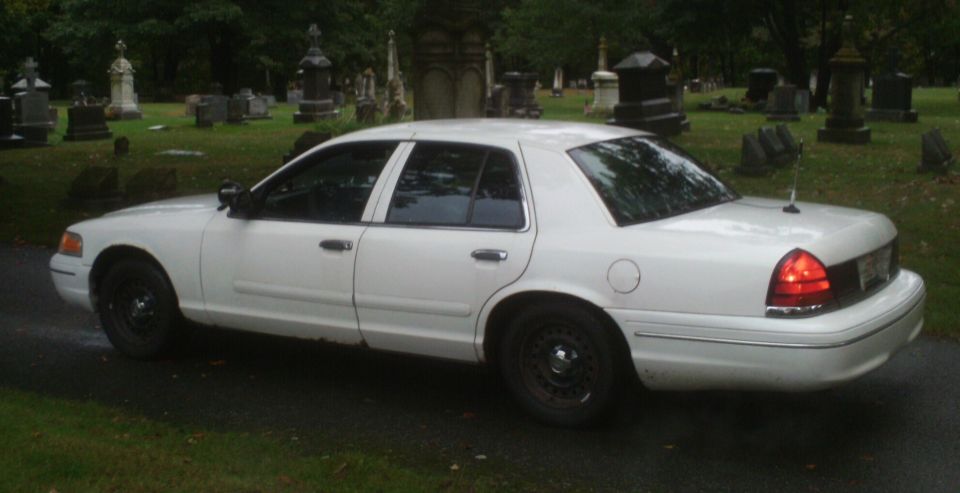 White sedan parked in a cemetery with gravestones in the background