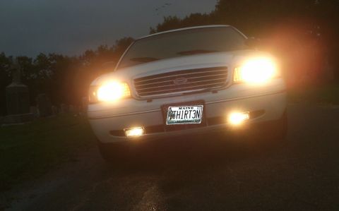 1998 Ford Crown Victoria - A white 1998 Ford Crown Victoria is shown from the front at dusk, its lights illuminated.