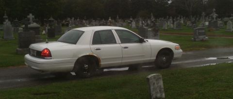 1998 Ford Crown Victoria - A white 1998 Ford Crown Victoria is seen driving through a cemetery on a cloudy day.