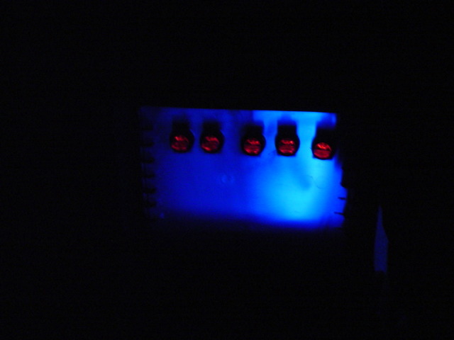 Five red indicator lights glowing under blue illumination inside a dark space