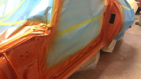 1973 Chevrolet Camaro - A car door is prepped for painting, with masking tape and plastic covering areas not being sprayed.
