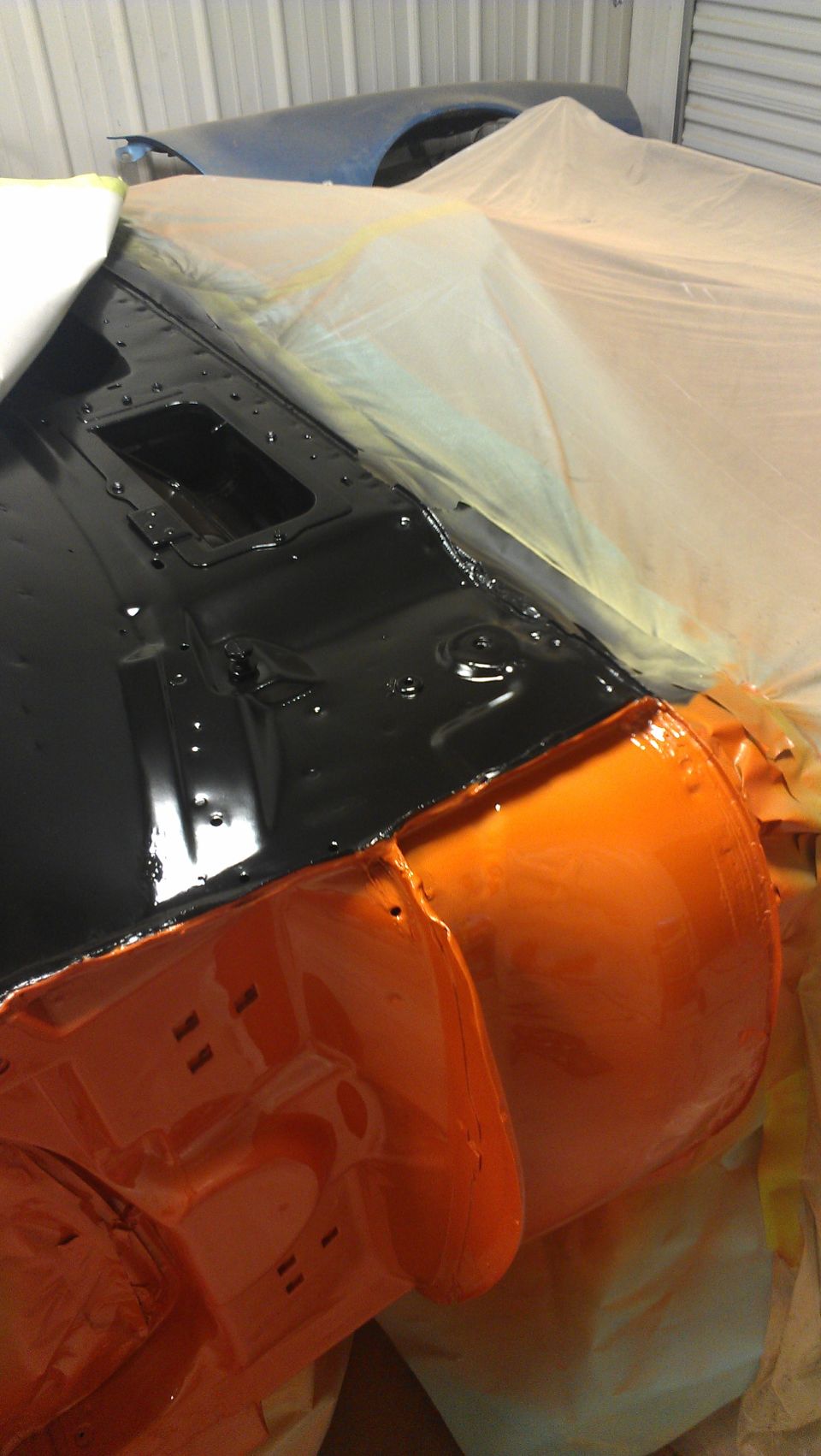 Car body parts with black and orange paint, covered in plastic sheeting