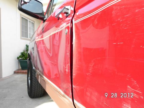 1994 Ford Bronco - The side of a red SUV shows significant scratches and scuffs, with a chrome trim piece along the bottom.