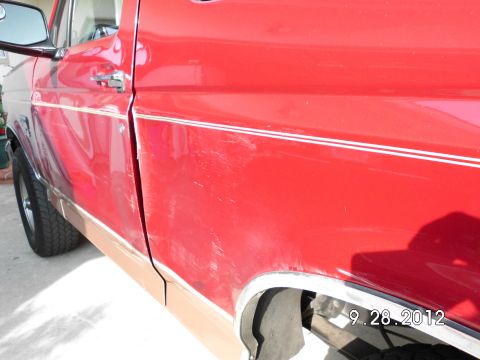 1994 Ford Bronco - The side of a red pickup truck shows significant scratching on the door and fender.