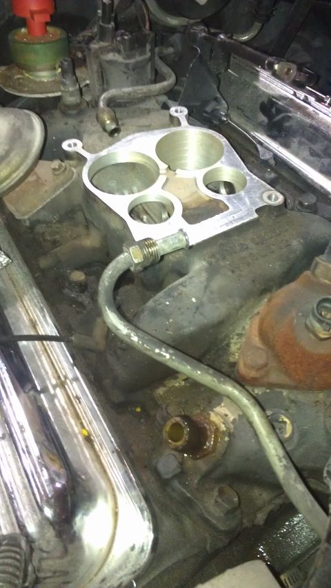 1973 Chevrolet Camaro - Close-up of an engine manifold and carburetor adapter plate, with a chrome valve cover on the side.