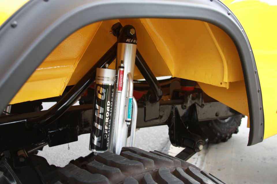 Yellow vehicle's rear wheel well interior with black fender flare, showing a King Off-Road shock absorber and part of a large tire