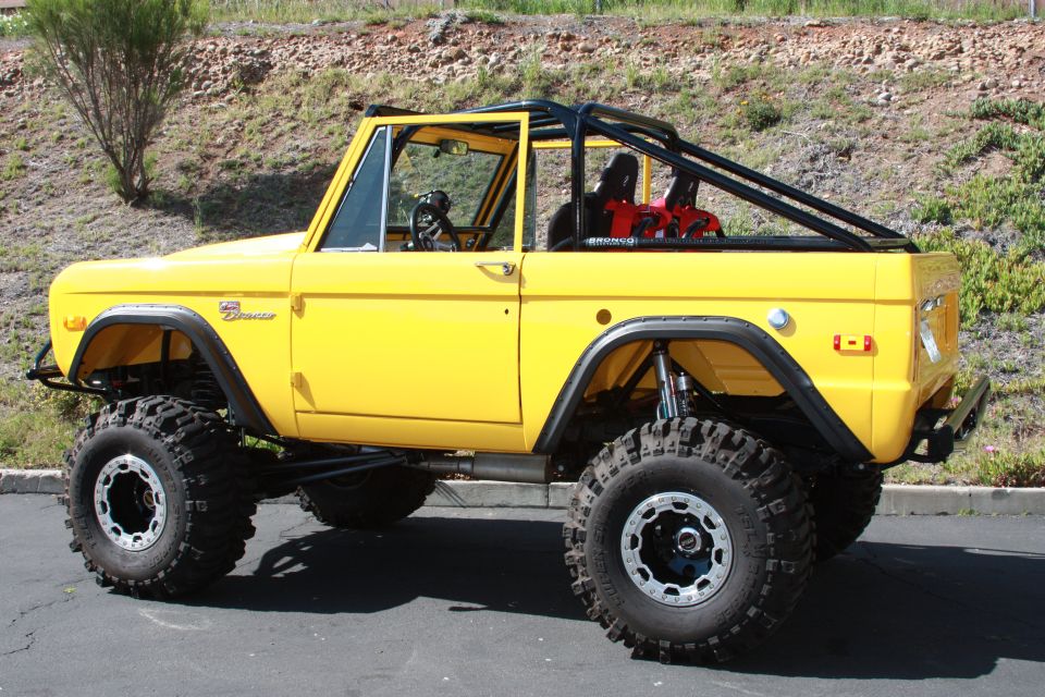 Yellow 1970 Ford Bronco with a roll cage and large off-road tires, viewed from the front three-quarter angle
