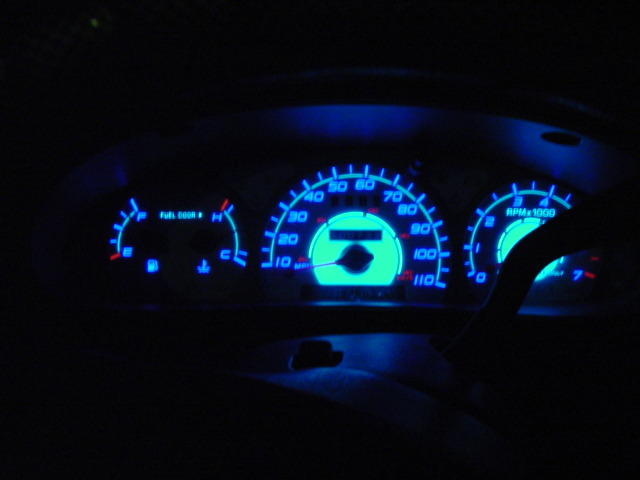 Car dashboard with glowing blue and green gauges, including speedometer and RPM meter, at night