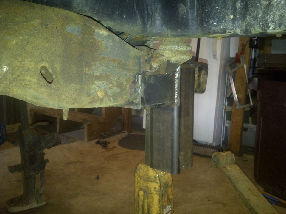 Welded steel bracket attached to rusty vehicle frame, supported by jack stands