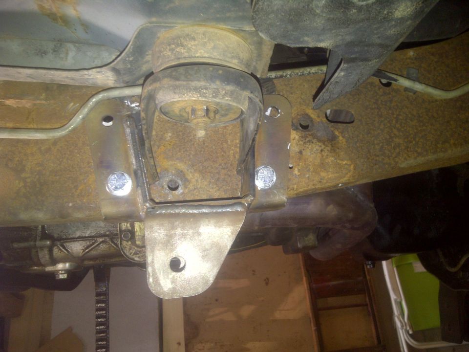 Close-up of a rusty vehicle frame with a newly welded, custom suspension bracket and bolts