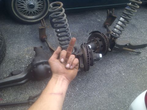 1995 Ford Bronco - Disassembled front axle components are laid out on asphalt, with a hand obscuring part of the view.