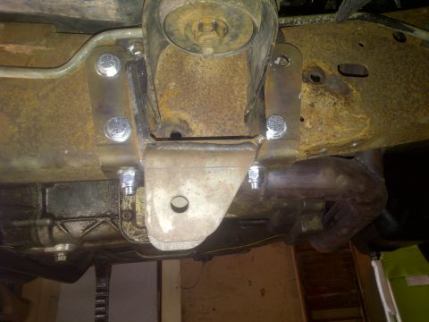 1995 Ford Bronco - Close-up view of a custom suspension bracket and exhaust pipe attached to a heavily rusted vehicle frame.