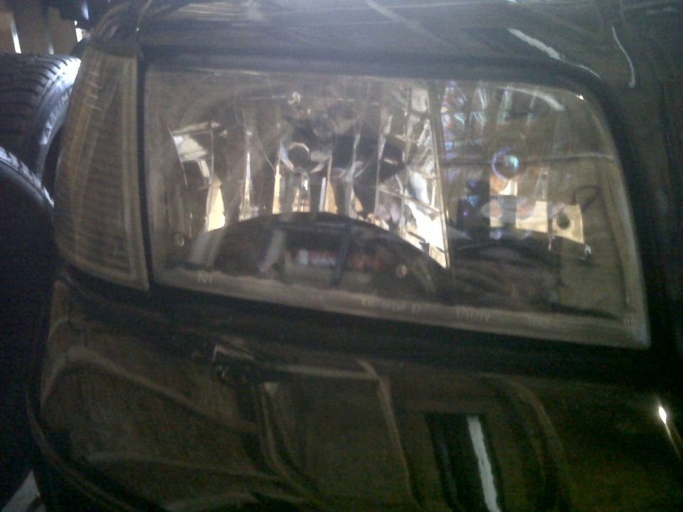 Close-up of a car's headlight and part of the fender. The headlight has a clear lens with multiple bulbs inside