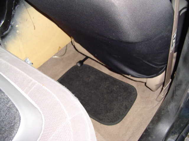 Interior shot of a car's passenger side floor with a black floor mat and tan carpet