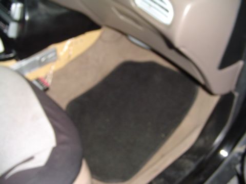 1999 Ford Taurus - The interior of a car shows a tan carpet and a black floor mat.