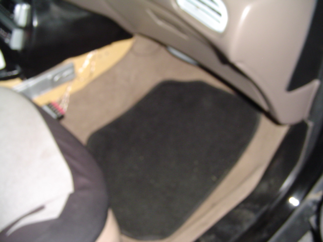 Car interior showing tan carpet, black floor mat, and part of a grey seat