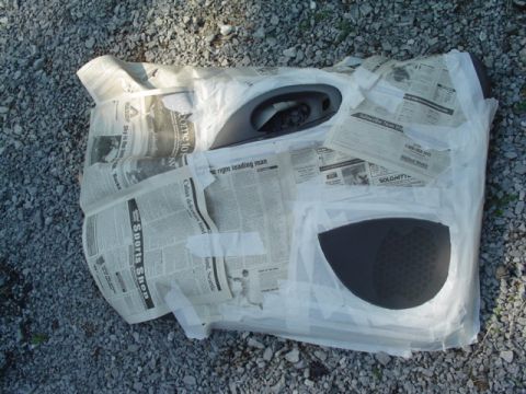 1999 Ford Taurus - A gray interior door panel lying face-up on a gravel driveway, masked off with newspaper and painter's tape so only the armrest/pull-cup po…