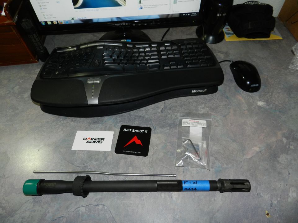 Gun barrel, Rainier Arms sticker, and computer keyboard and mouse on a desk