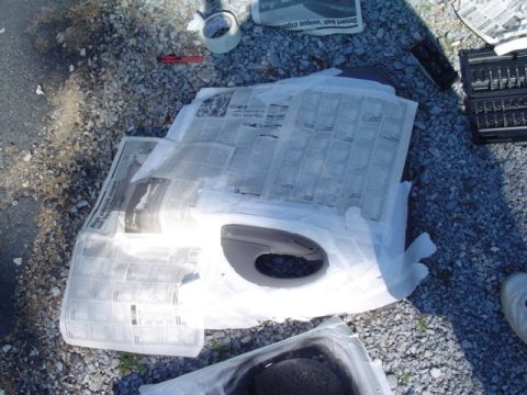 1999 Ford Taurus - plastic interior or trim piece masked with newspaper and tape, set on gravel for spray painting alongside tools.