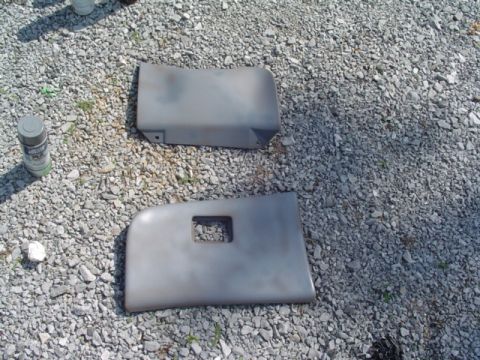 1999 Ford Taurus - Two grey interior dash trim panels, one a glovebox door with a recessed latch pocket, laid face-up on a gravel driveway during refinishing.…