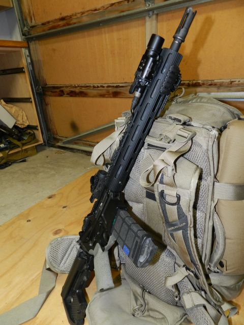 1996 Ford Bronco - Tactical rifle with flashlight and scope, placed on a backpack in front of a garage door.