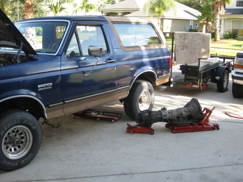 1994 Ford Bronco - A blue Ford Bronco is undergoing maintenance, with its transmission removed and placed on jacks next to the vehicle.