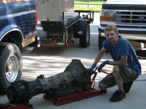 1994 Ford Bronco - A man works on a transmission next to a 1994 Ford Bronco and another truck.