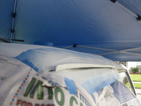 1994 Ford Bronco - Roof of a white vehicle masked with paper and blue tape for painting under a blue pop-up canopy.