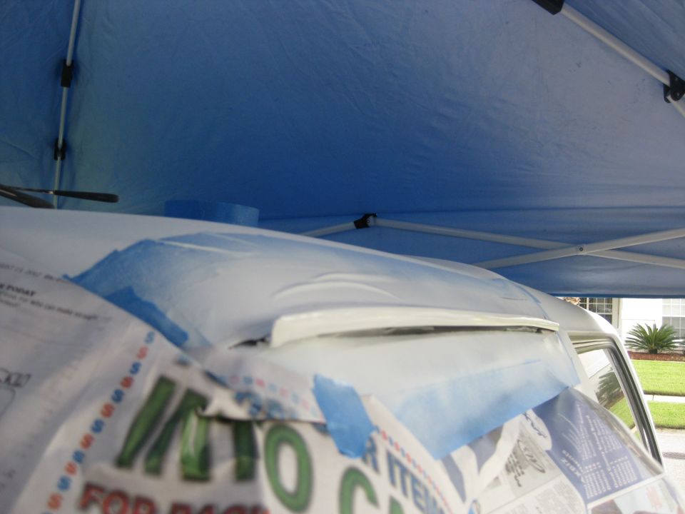 White vehicle roof being prepped for paint with masking paper under a blue canopy